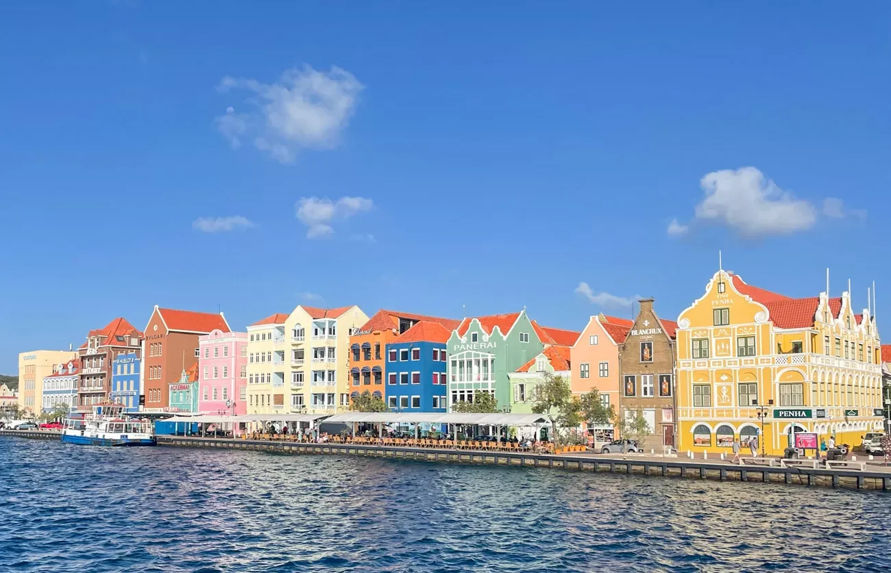 Rij kleurrijke huizen in Willemstad, ook bekend als Handelskade, genomen vanaf de Pontjesbrug, Sant Anna baai voor de huizen vlakbij Willemstad Cruise Port
