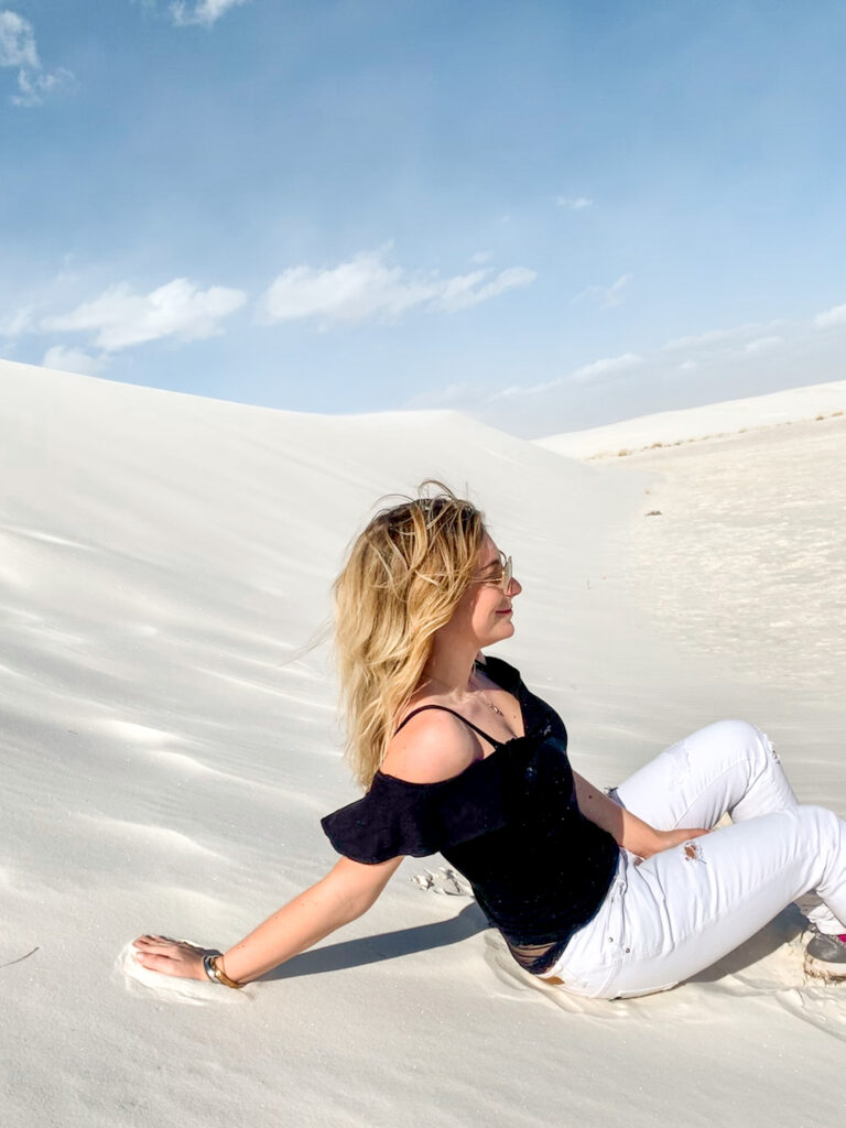 Blonde girl at White Sands National Park in New Mexico sitting in the dunes