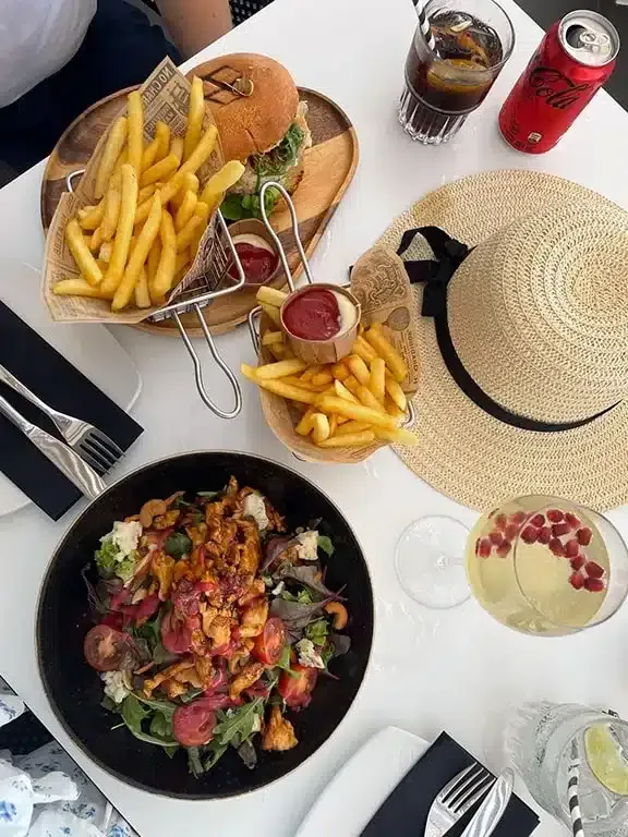 Lunch in Saint Tropez Ocean club, salade, cocktails en een hamburger met frietjes op tafel