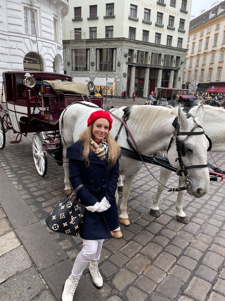Blonde girl with two horses in front of horse carriage on Michaelerplatz in Vienna in winter