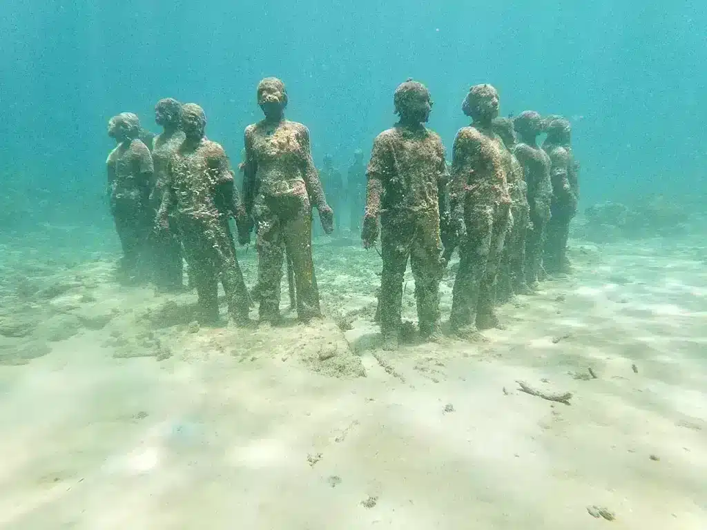 Underwater sculptures standing in a circle in Grenada with fish swimming around them