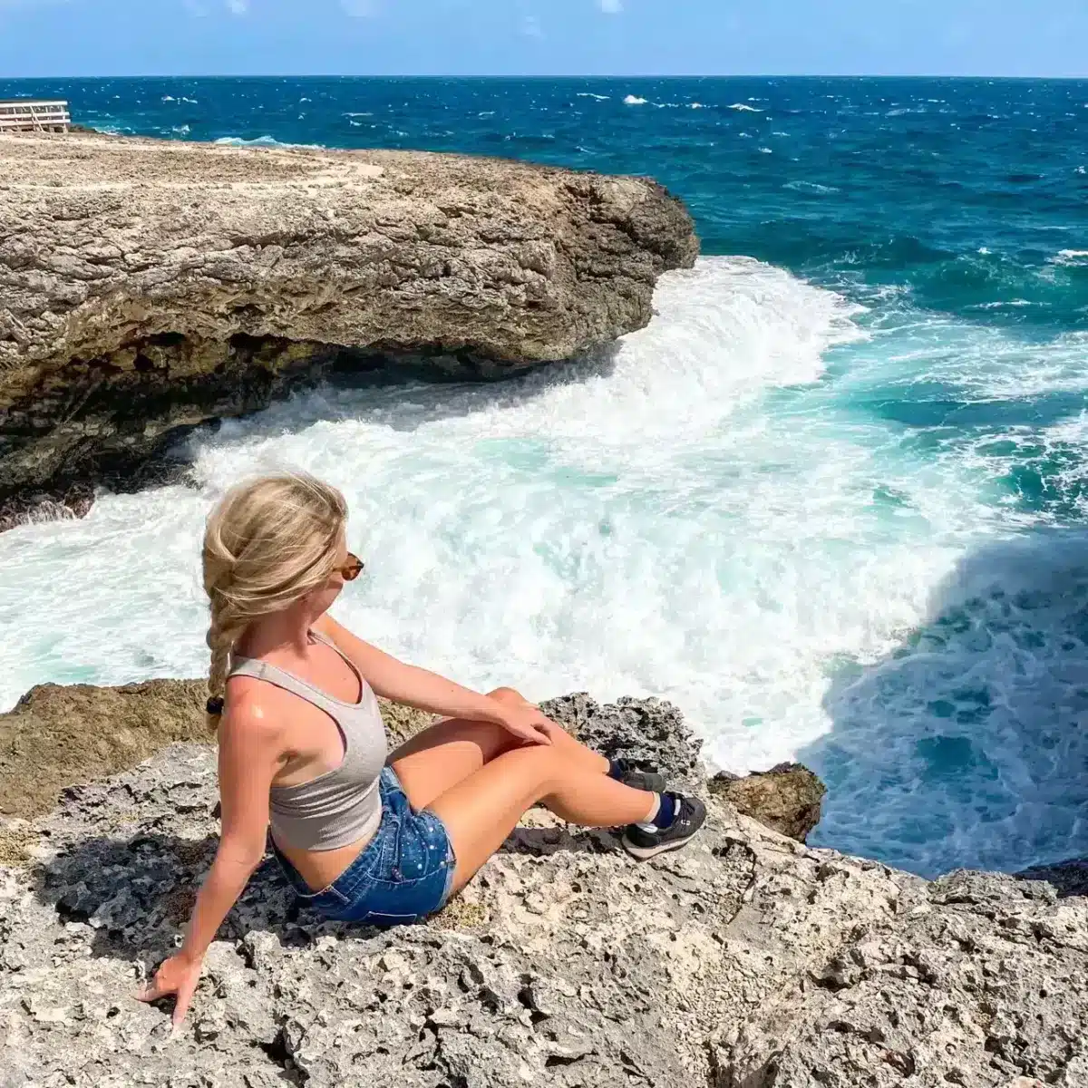 the author sitting on the edge of a cliff overlooking stunning big waves and blue water