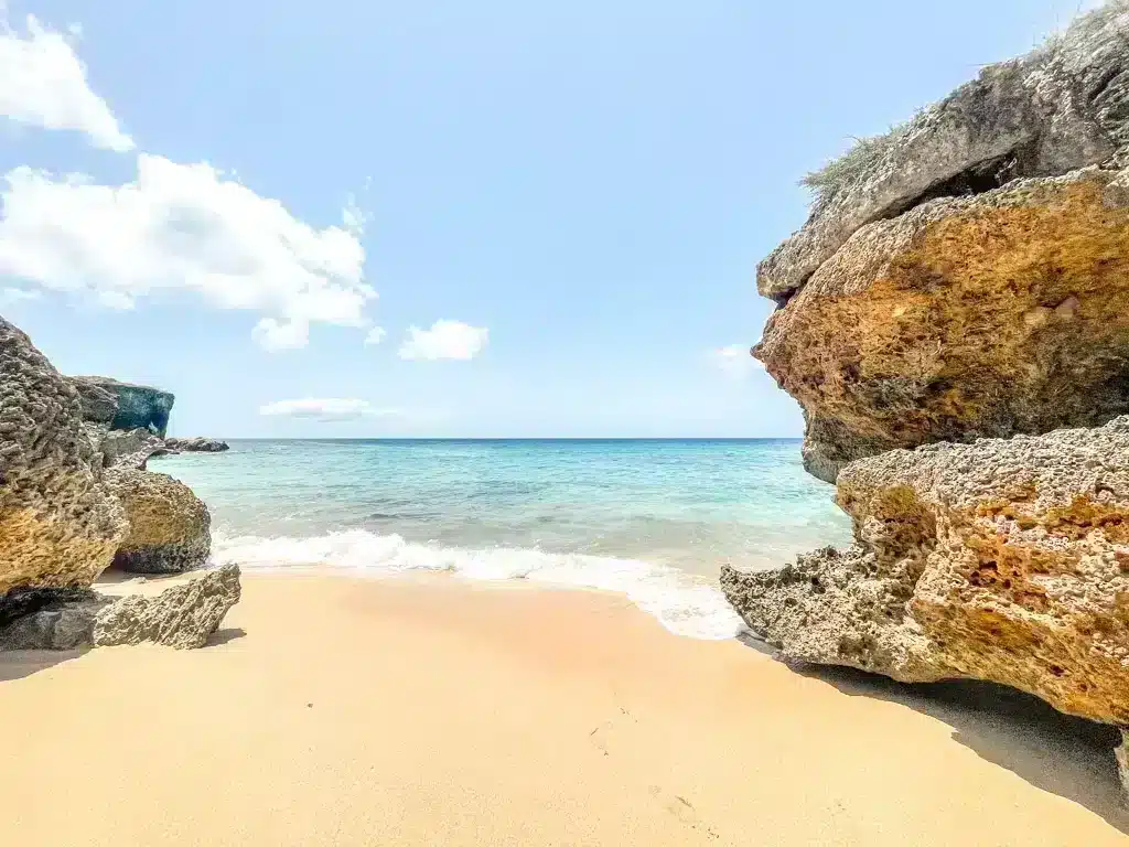 Abandoned small beach with white sand and blue ocean in between cliffs