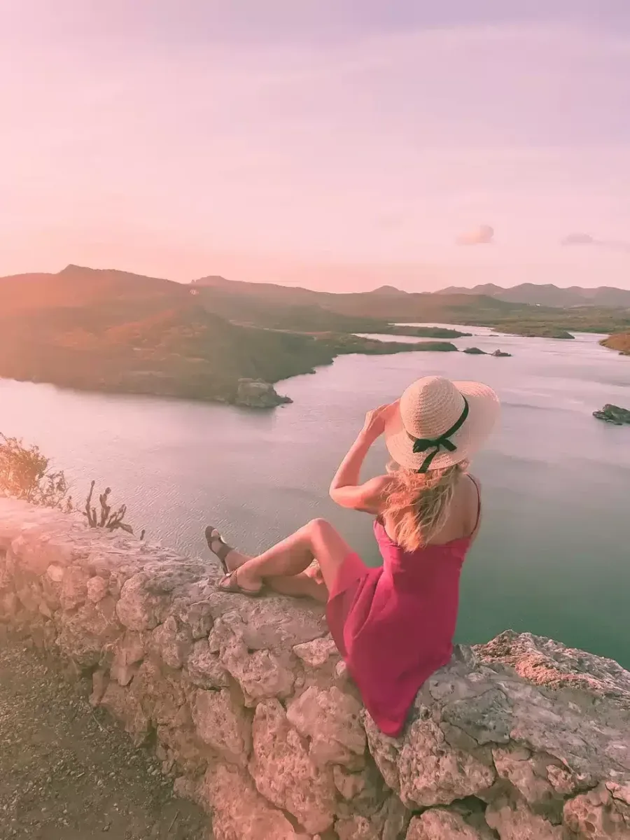 Santa martha Lookout point in Curacao at sunset with a girl standing on a rock overlooking the pink sky