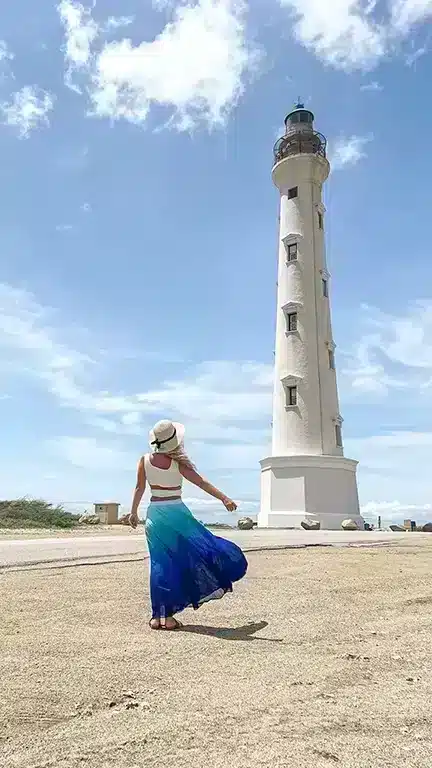 Girl standing in front of California Lighthouse in aruba with a flowing blue skirt that is waving in the wind