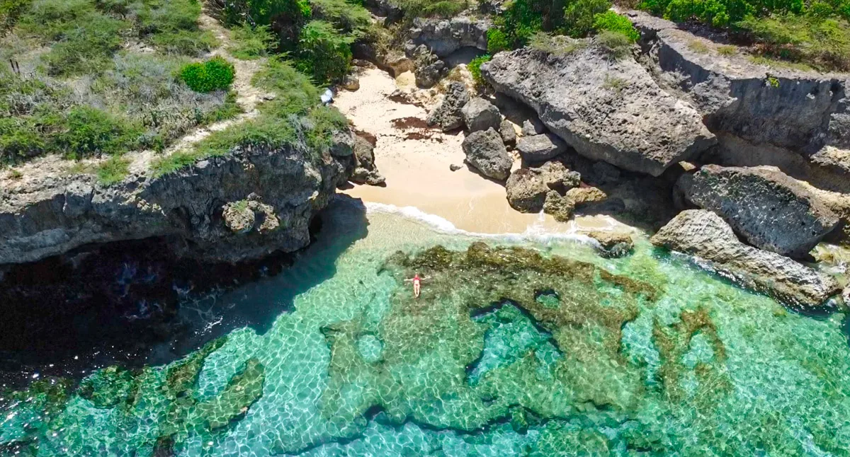 stunning drone shot of the hidden beach playa gipy in curacao with the author floating in the water in a red bikini 