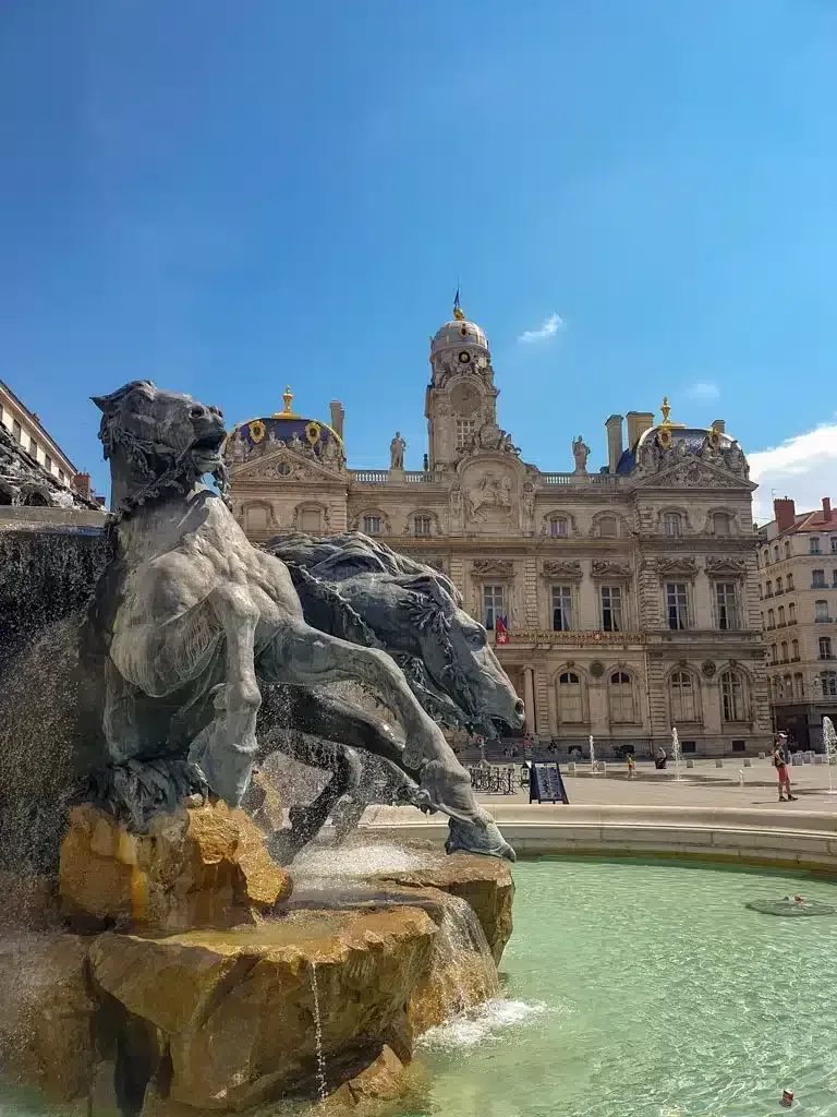 Picture of a castle in Lyon France with a fountain of horses in front of it 