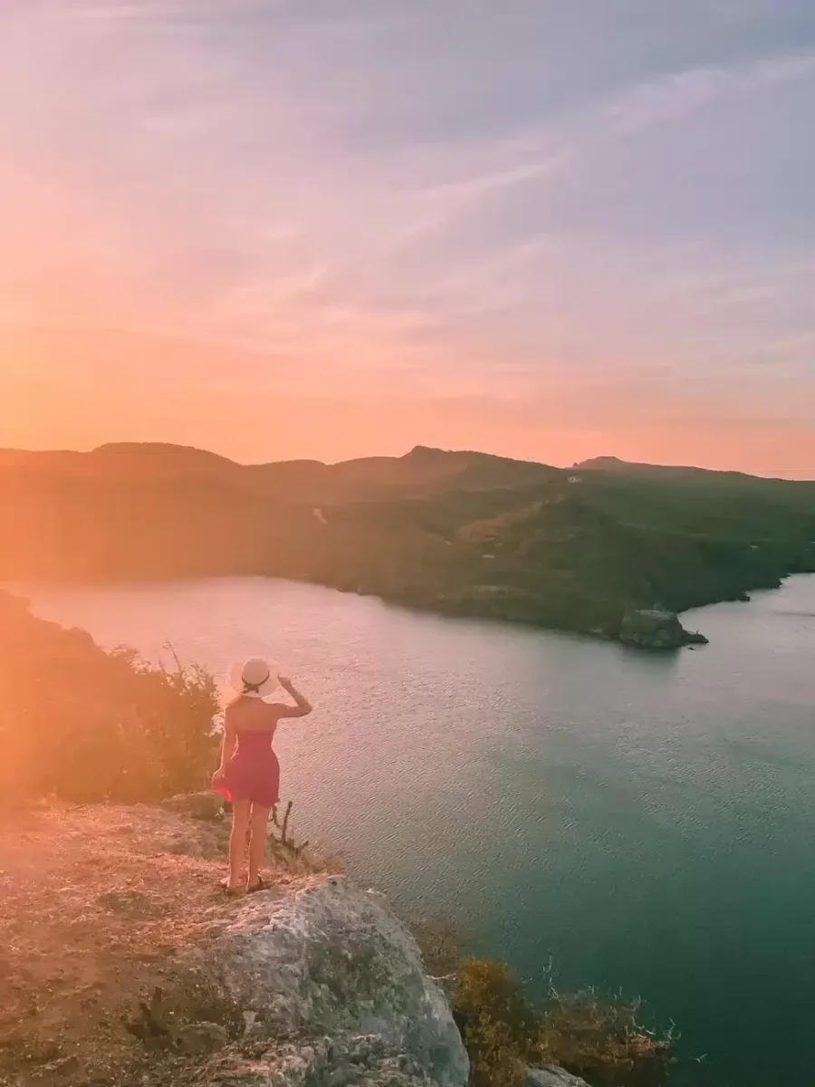 Santa martha Lookout point in Curacao at sunset with a girl standing on a rock overlooking the pink sky