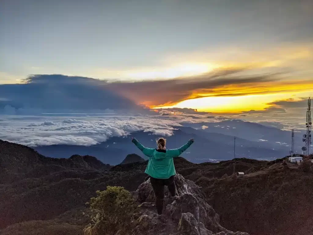 Girl standing on top of a hill overlooking sunset over a volcano with a beautiful colored sky 