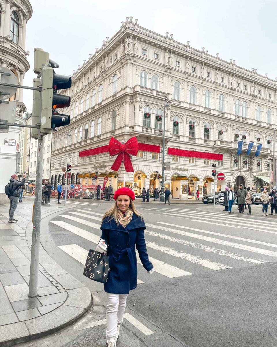 The author walking in vienna in a coat in front of a building decorated with a red bow for Christmas