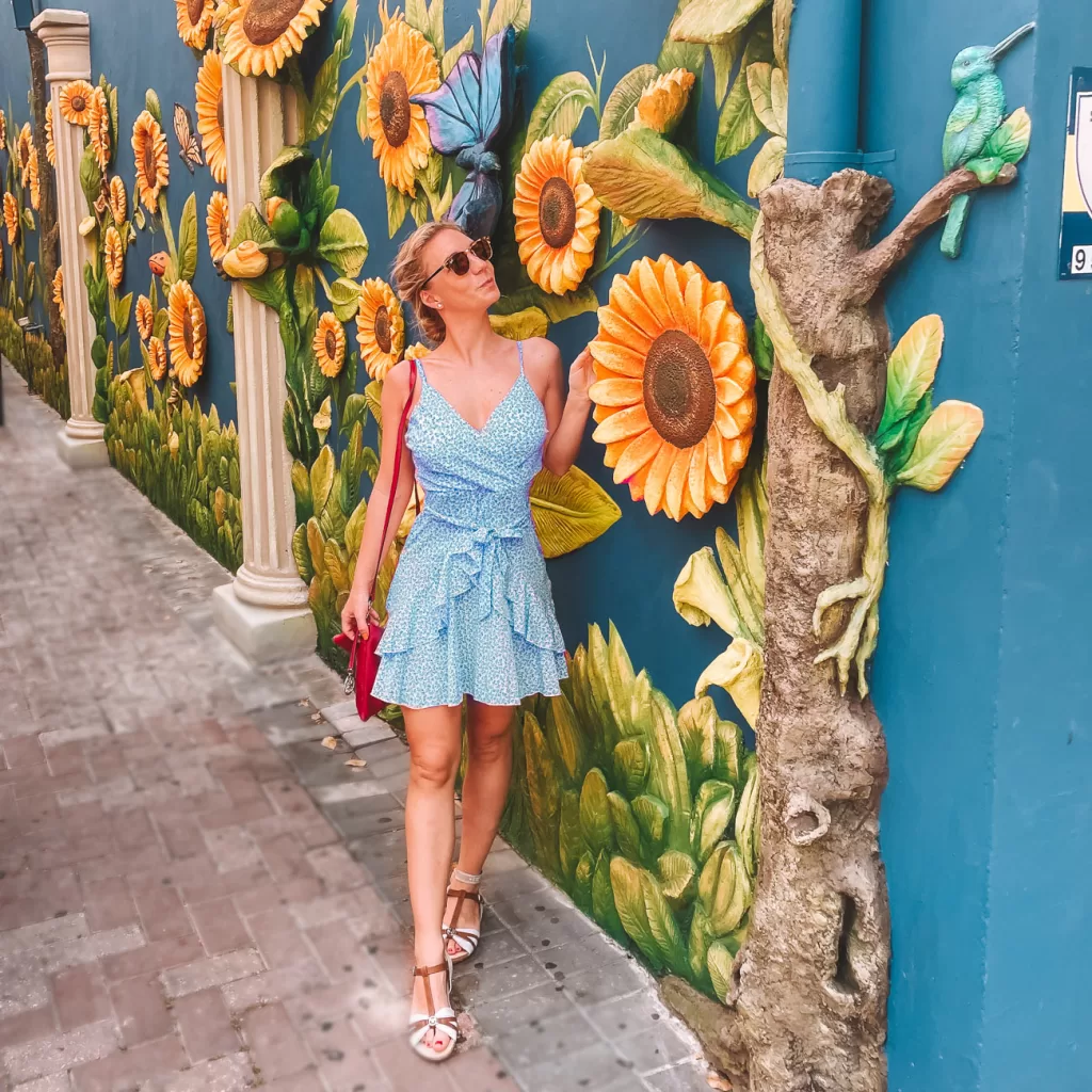 Beautiful mural made of orange, pink and many other colors with flowers and patterns and author standing in a dress in front of it 