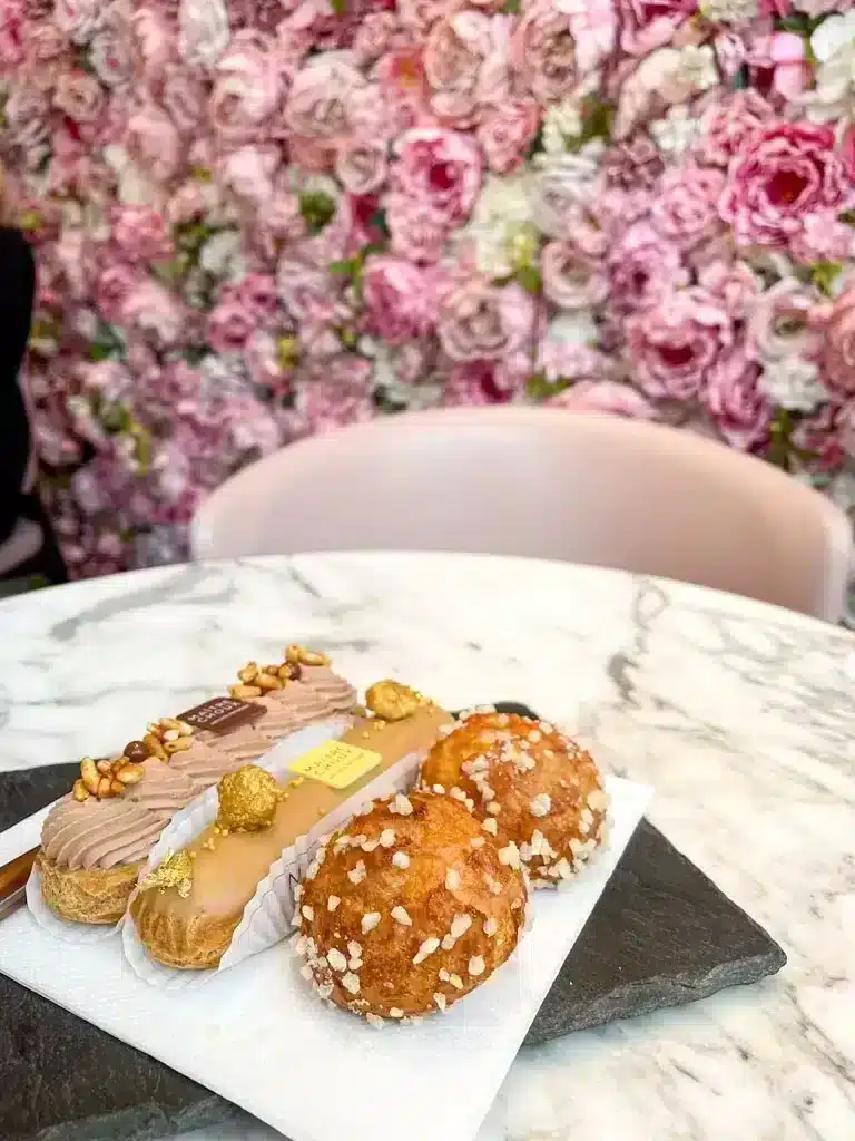 Pink wall of flowers with matcha latte and eclairs at Maitre Choux cafe in London 