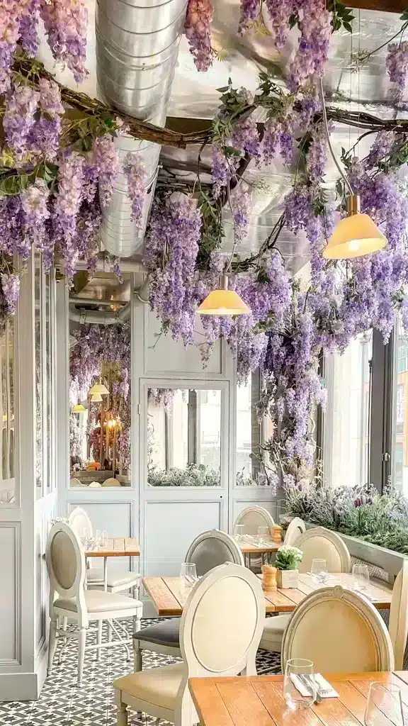 A cafe with lots of tables and empty glasses and cutlery with wisteria hanging from the ceiling 