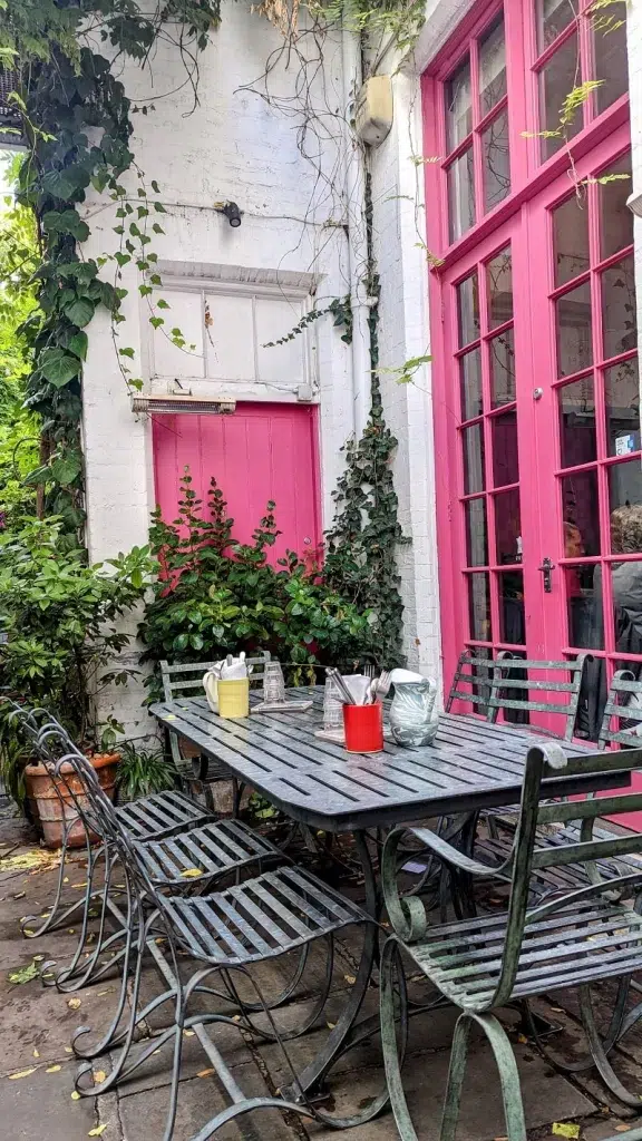 Cafe with pink doors and garden furniture in front of it in London 