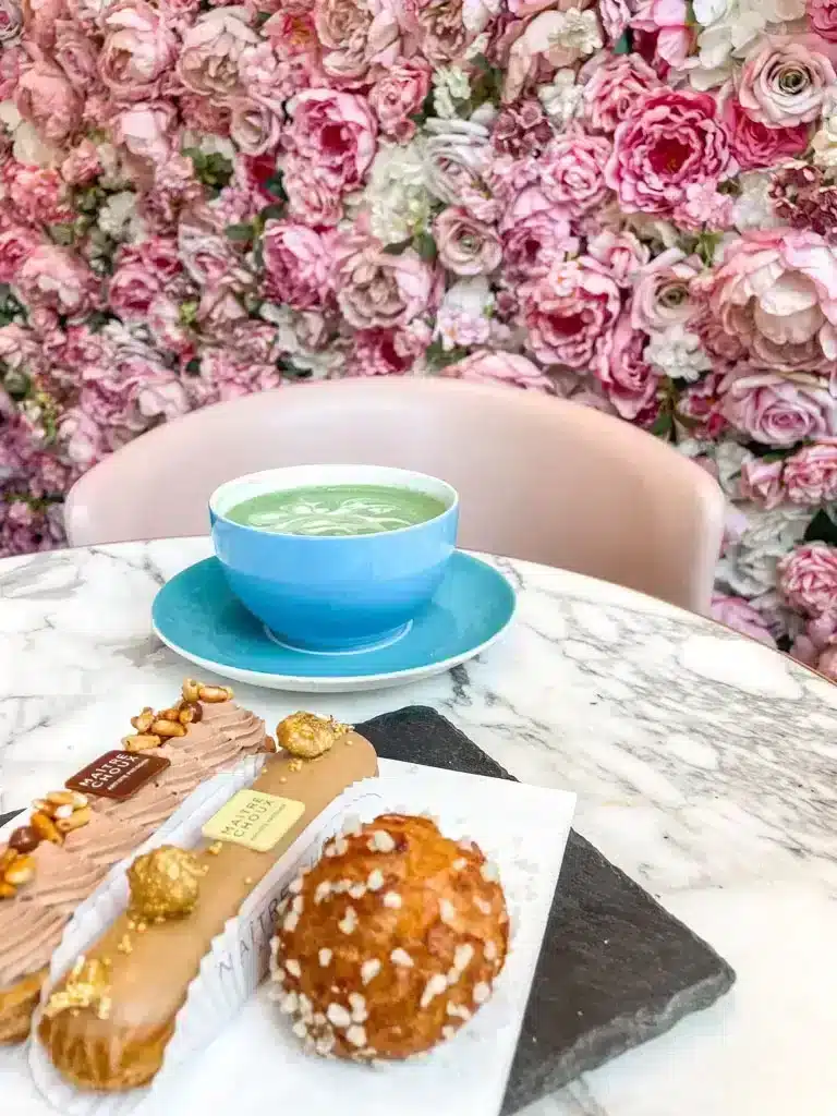 Pink wall of flowers with matcha latte and eclairs at Maitre Choux cafe in London 