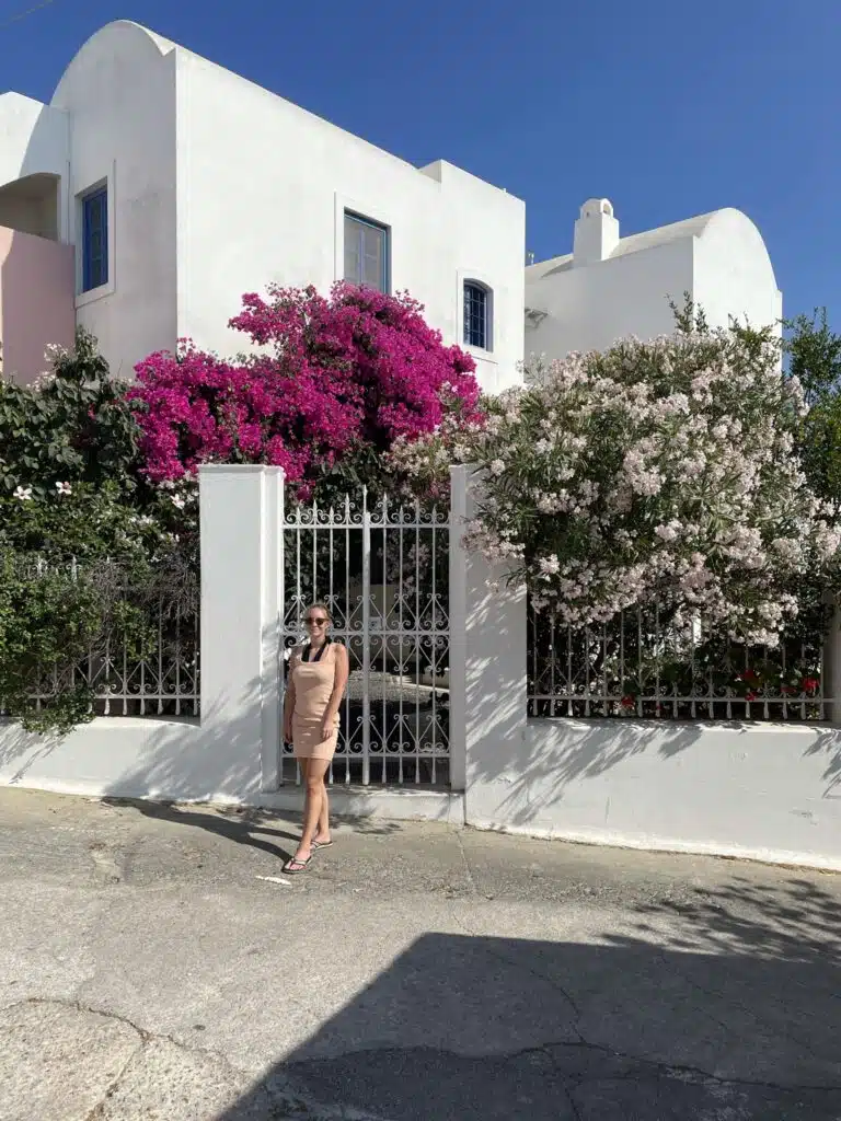 The Author in a pink dress in front of a cute house with pink flowers in Pyrgos
