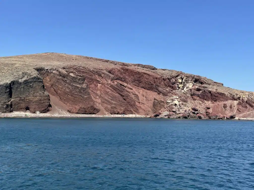 Picture of huge red cliffs on red beach in Santorini taken from a boat
