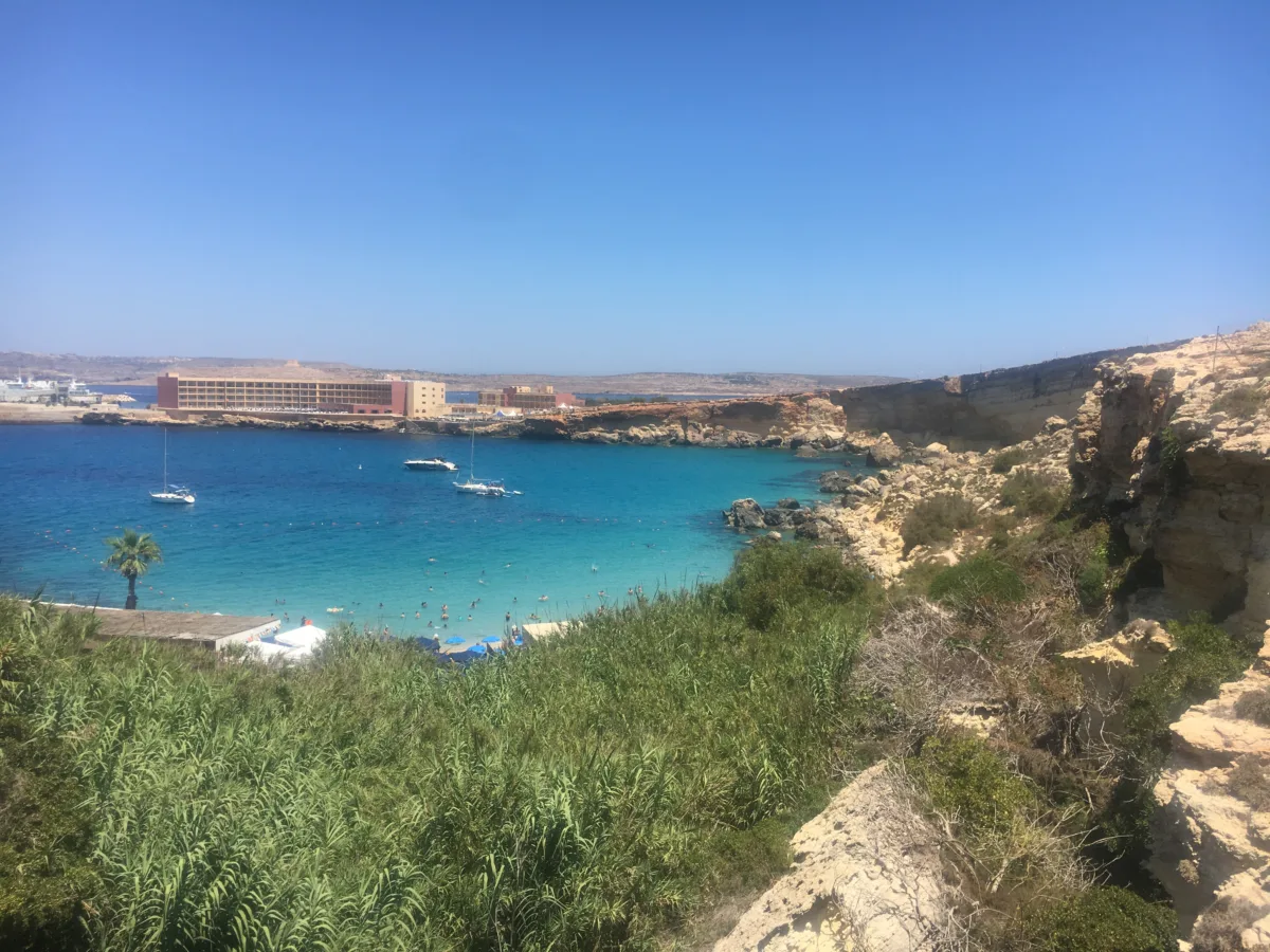 a beach from above in Malta with blue water and luxury hotel in background