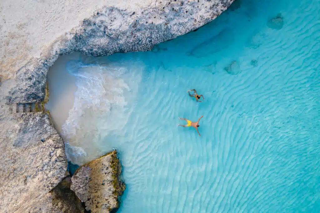 Drone shot of two people swimming and snorkeling in a small bay in light blue water in Aruba