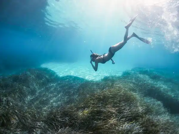 girl snorkeling underwater toward coral reefs