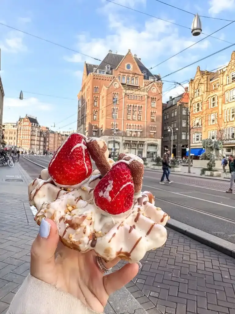 a waffle with strawberries and chocolate held up high in front of Amsterdam building