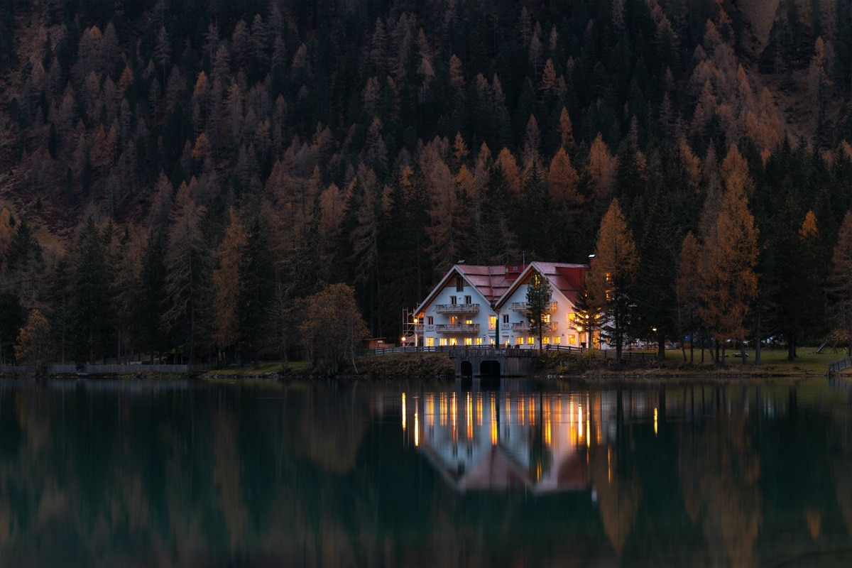 house in the forest on a lake in the evening with lights on 
