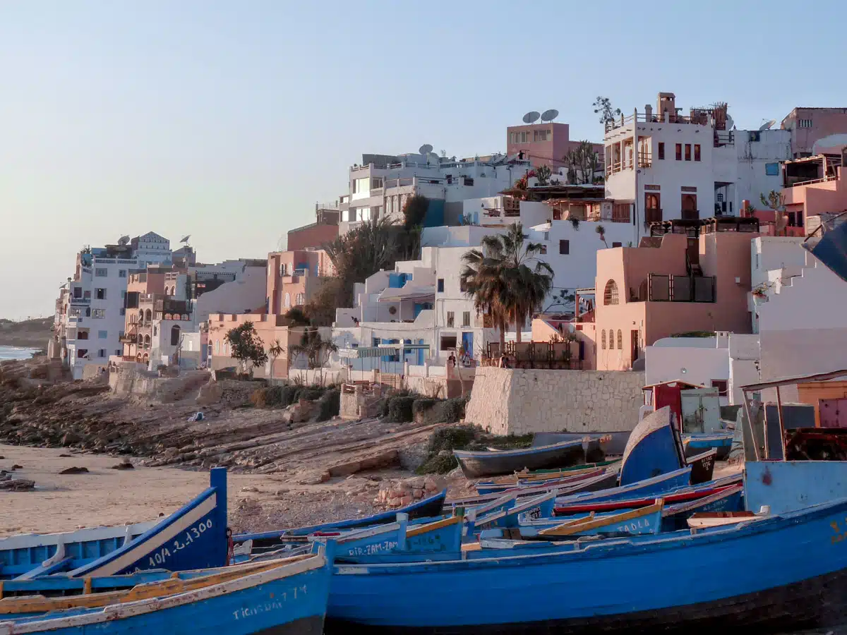Picture of white and pastel colored houses on a cliff at sunset with some fisher boats in front of it