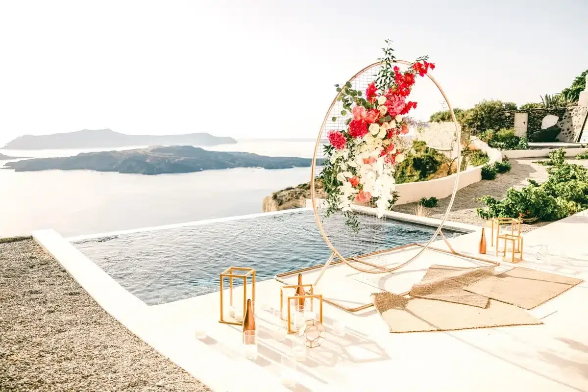 beautiful wedding arch filled with pink flowers in front of an infinity pool overlooking santorini caldera for destination wedding