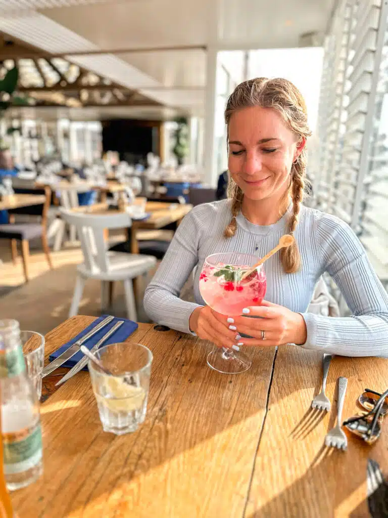 The author smiling and sipping a gin tonic with red berries at a restaurant called the waterreus in Scheveningen