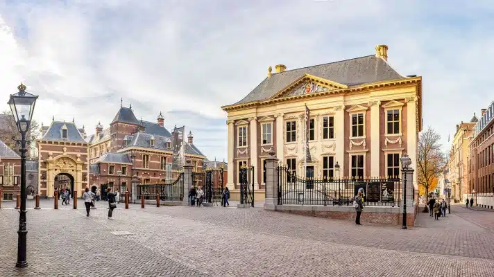 The famous Mauritshuis in the Hague with some people walking in front of it and the Binnenhof in the background