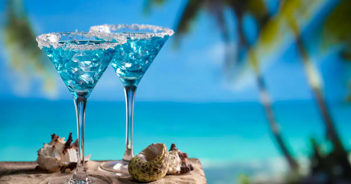 two blue curacao cocktails in front of beach in curacao