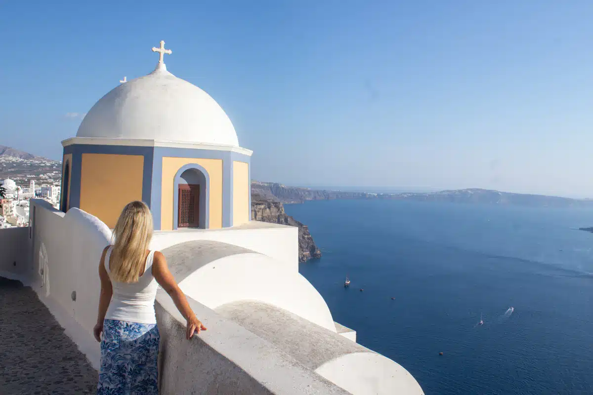 author next to a beautiful blue domed church in santorini