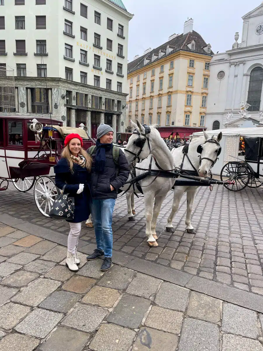 the author and her husband posing with a horse in vienna in front of a traditional carriage