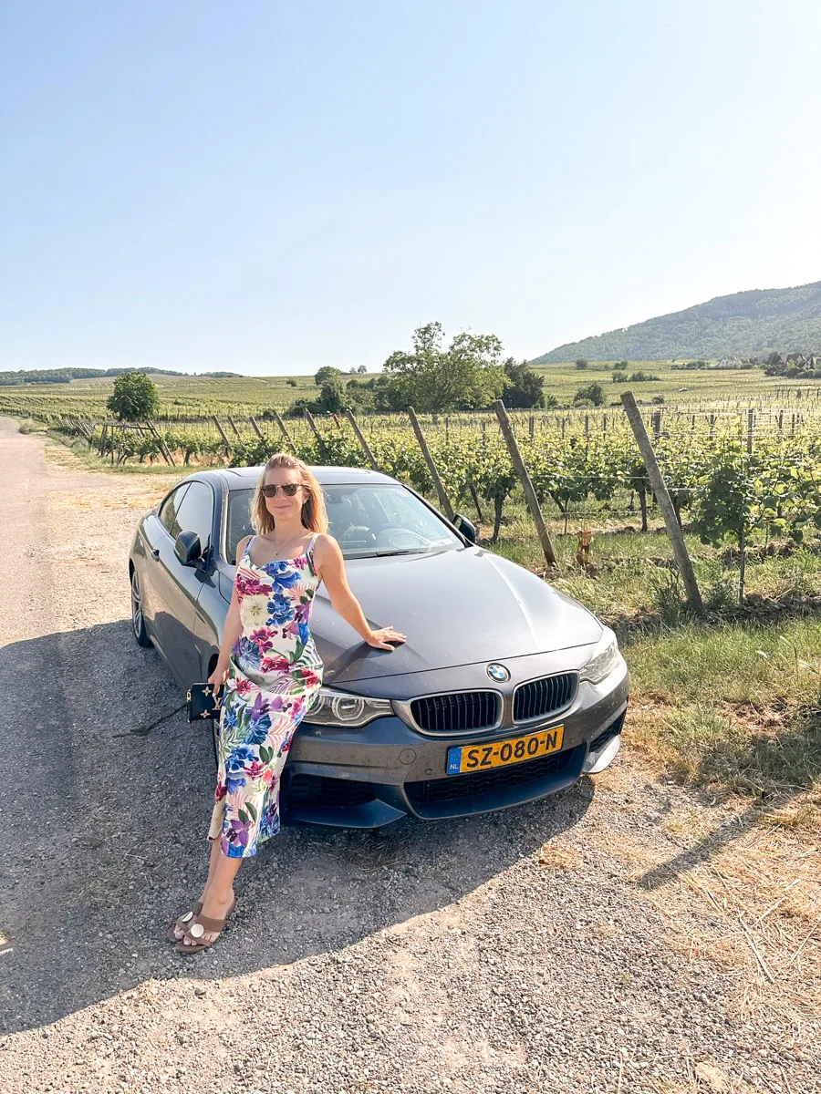 the author sitting on the hood of a bmw in front of vineyards 