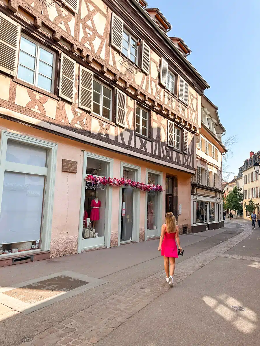 the author posing in a short pink dress in alsace in front of storefront in spring