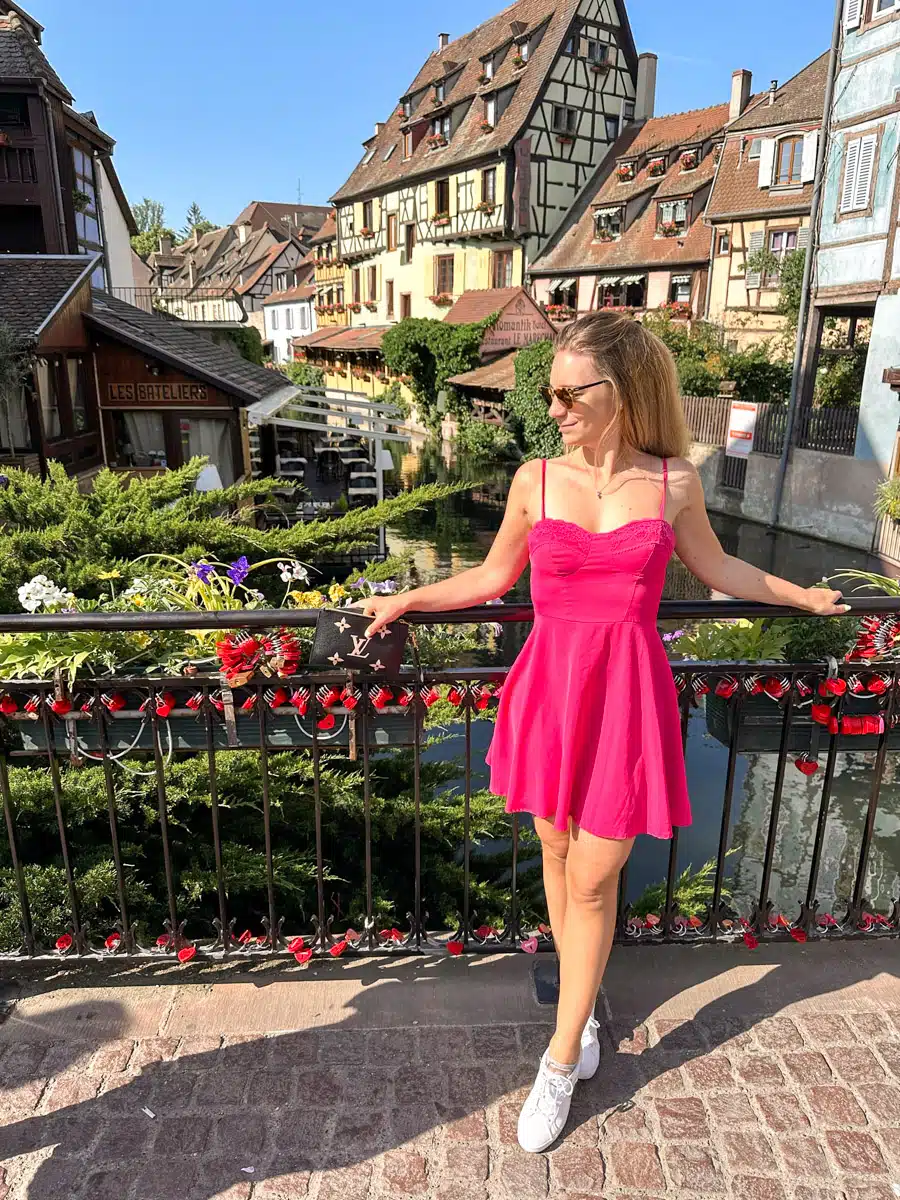 the author posing in front of a river in colmar in a pink dress