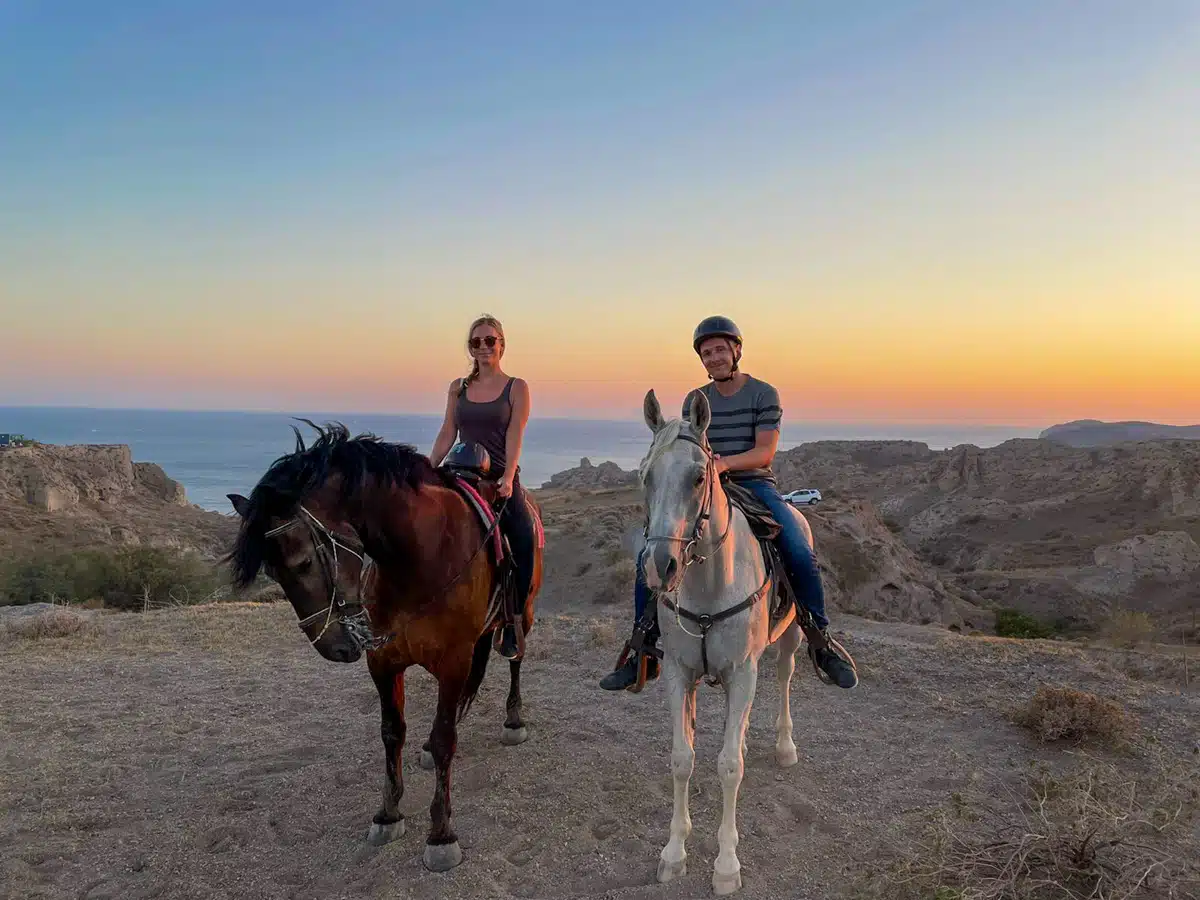 author and her husband riding horses in santorini at sunset for an instagram picture