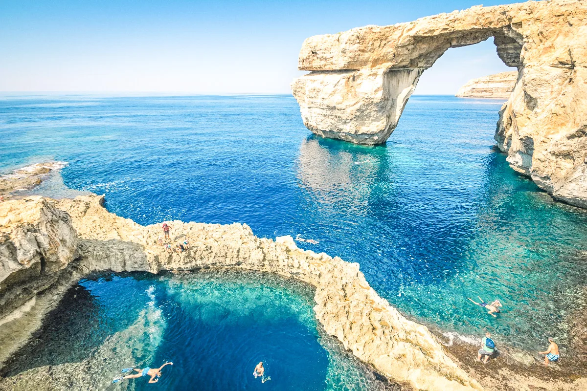 azure window in malta with people swimming in front of it 