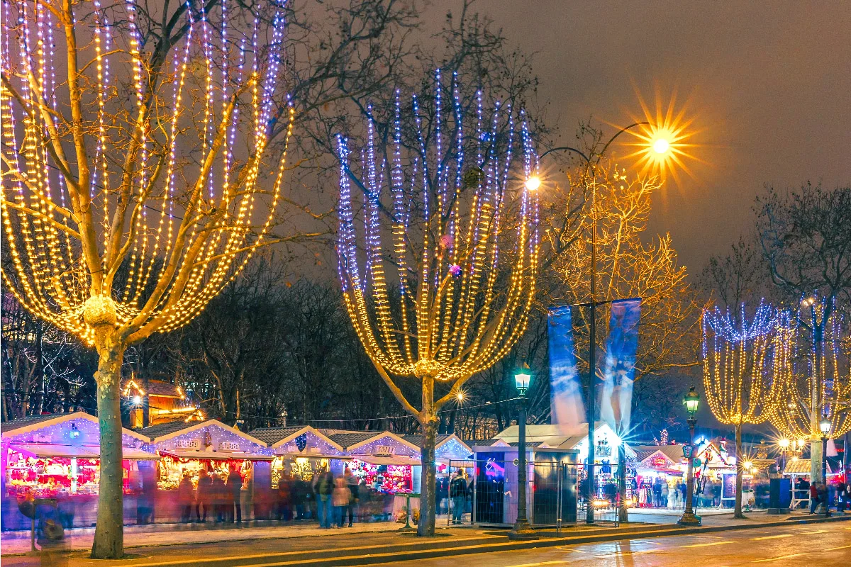 picture of decorated trees in paris with a small christmas market behind it 