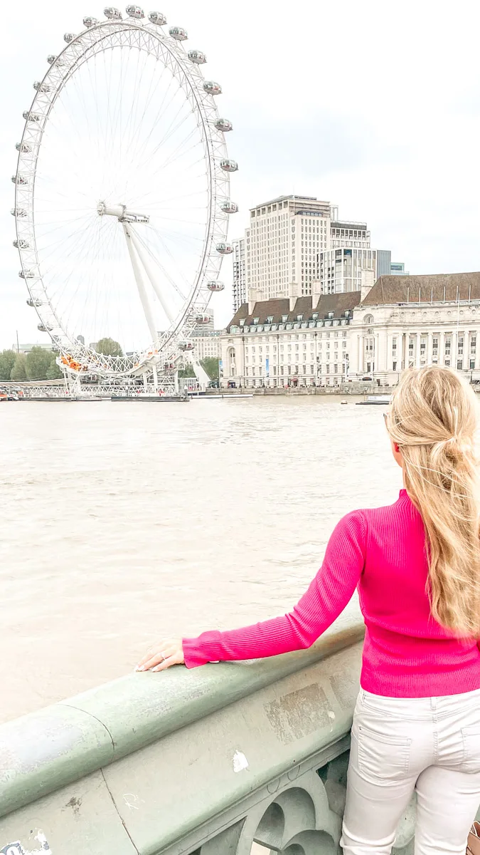 the author next to the london eye ferris wheel in a pink sweater