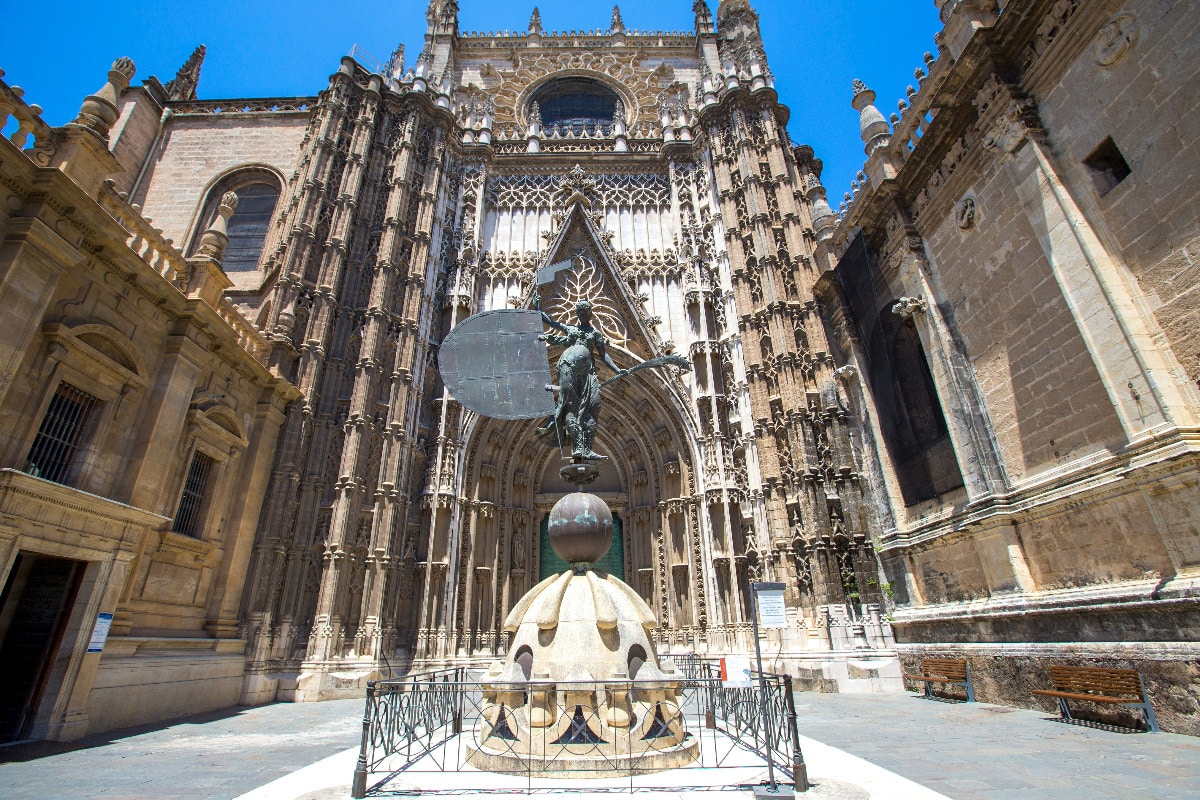 stunning cathedral in sevilla from the outside with a sculpture in front of it.