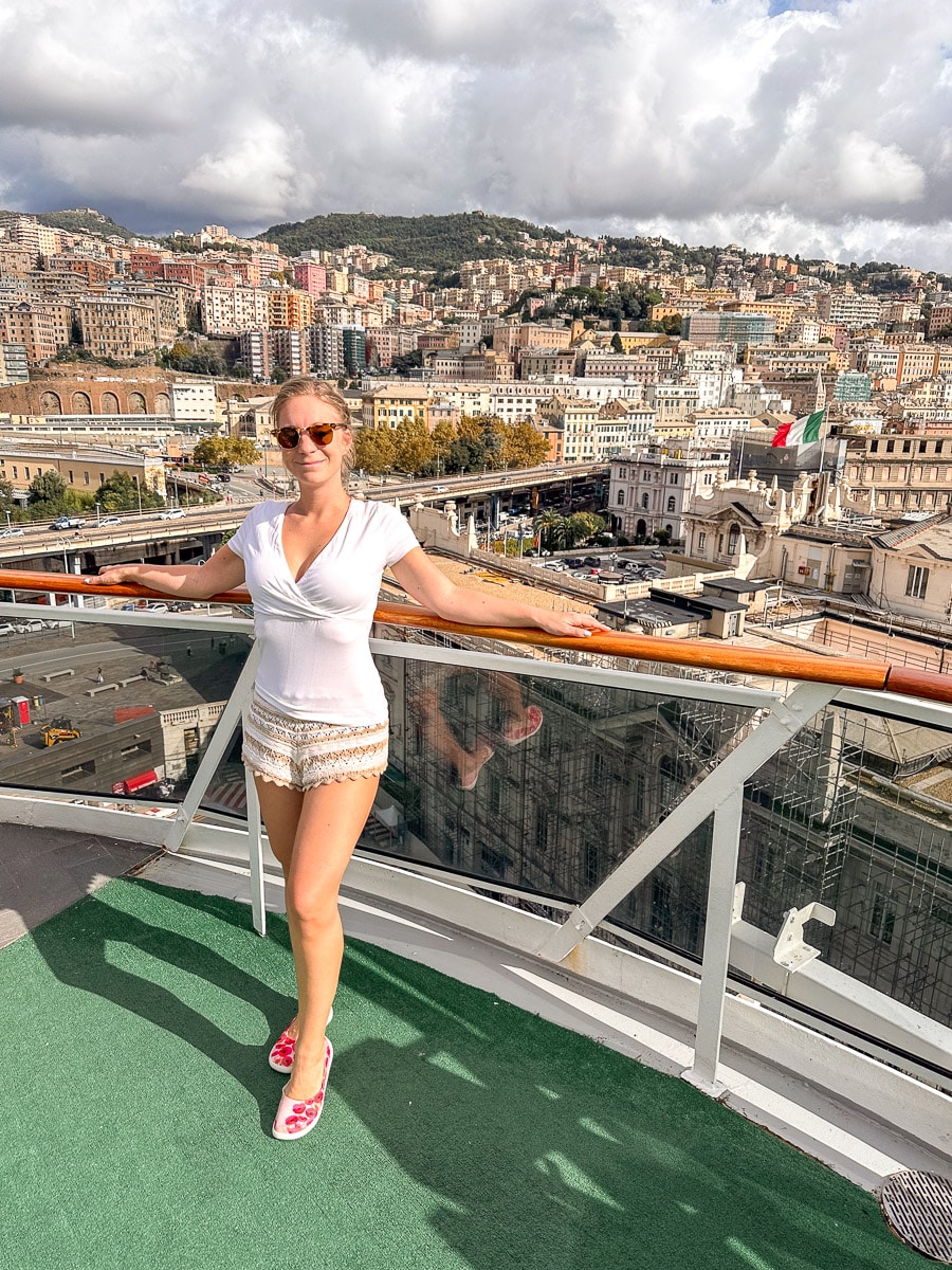 the author standing on the deck of the msc divina with the beautiful houses of genoa in the background