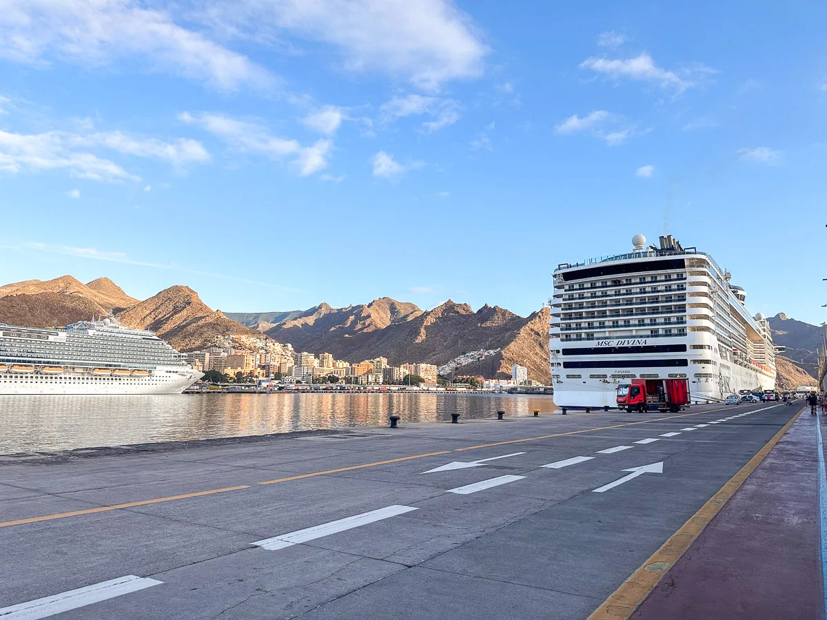 
This image features the MSC Divina cruise ship docked at the port in Santa Cruz de Tenerife. The vast ship stands prominently against the clear blue sky, with Tenerife’s distinctive rugged mountains in the background. The port area appears quiet with few people, and the calm sea reflects the warm glow of the setting sun, emphasizing the serene and welcoming atmosphere of the island for its visitors.
