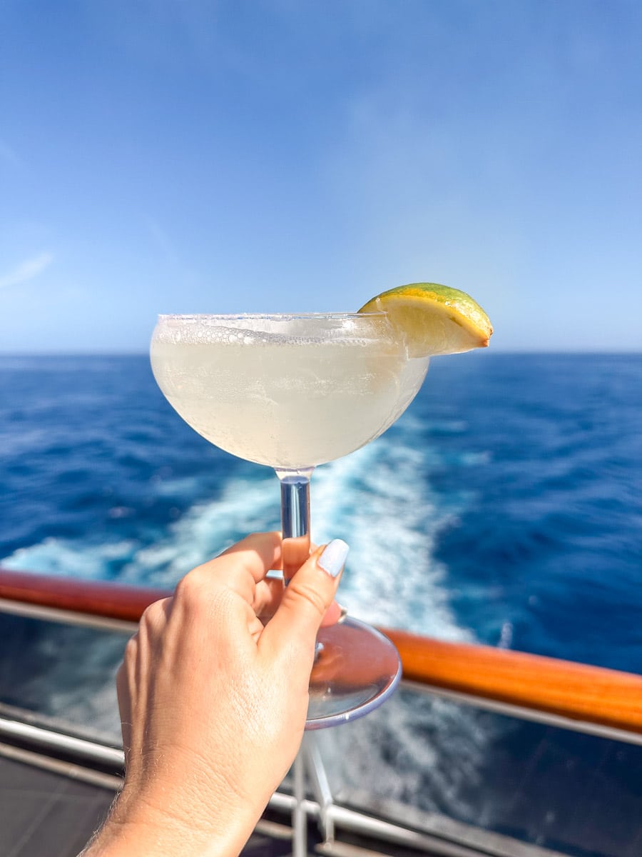 author holding a cocktail over the ocean from the msc divina
