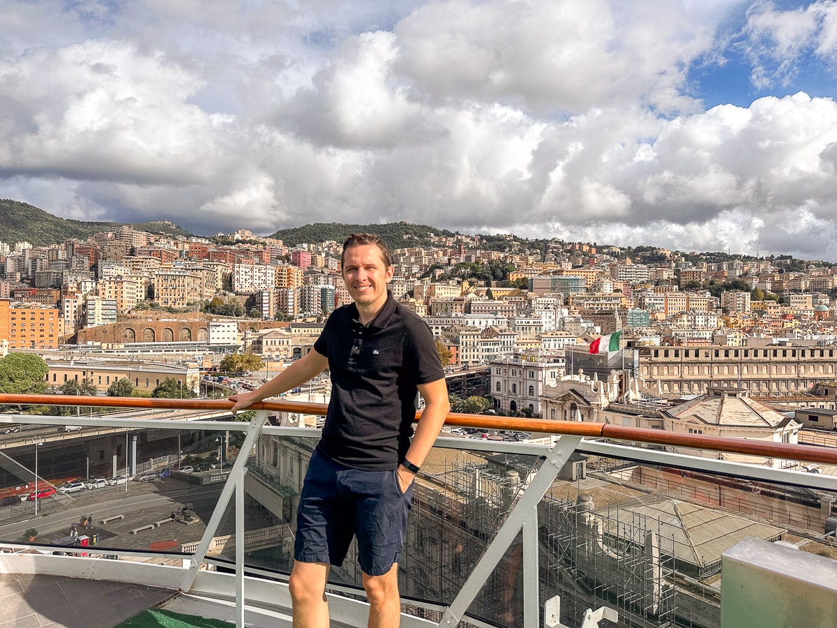 the authors husband standing on the deck of the msc divina with the beautiful houses of genoa in the background