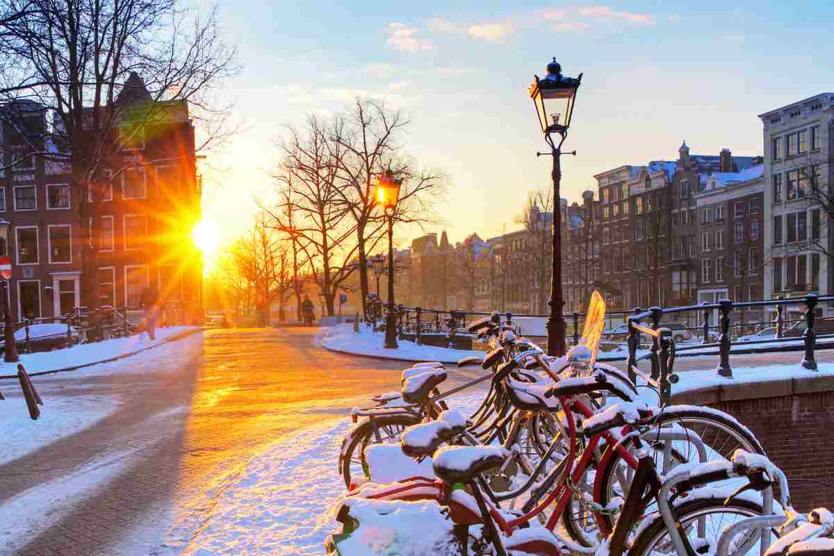beautiful picture of amsterdam in winter with bikes covered in snow and the sun slowly rising in the city