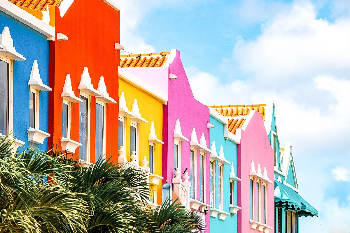A row of brightly colored, Dutch-style buildings in Bonaire, with intricate architectural details and a variety of vivid hues that pop against the blue sky