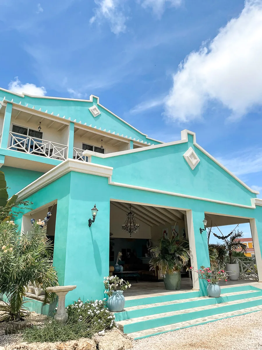 A vibrant turquoise-colored house with a welcoming open veranda, typical of Bonaire's colorful architecture, under a clear sky.