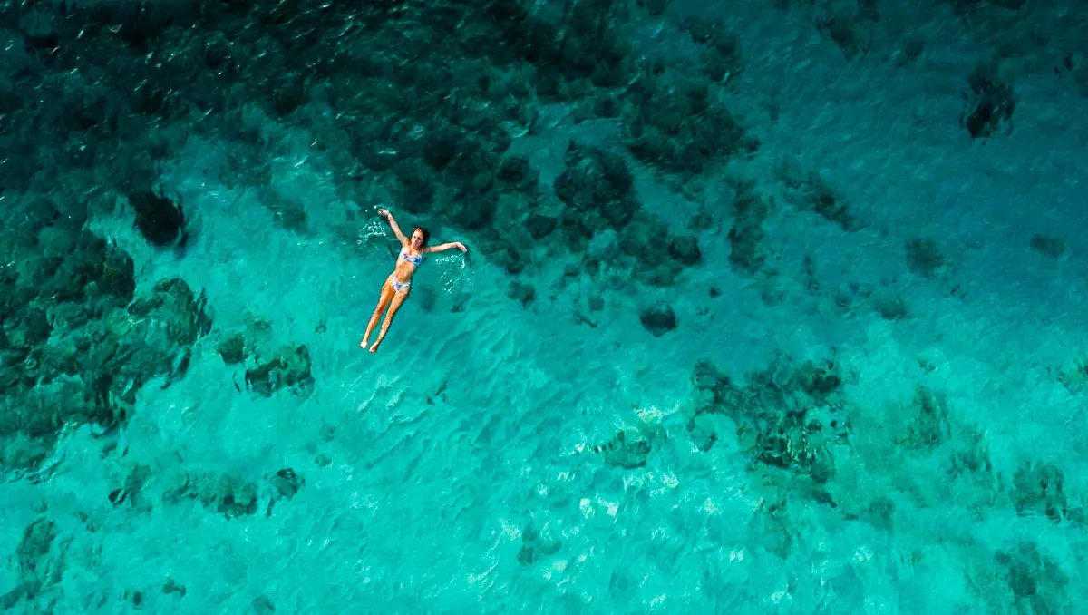 ocean drone shot with the author floating in the clear blue water at daaibooibay