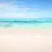 Pristine sandy beach meeting the crystal-clear turquoise waters of a calm sea, under a beautiful sky with soft clouds, creating a serene tropical scene.